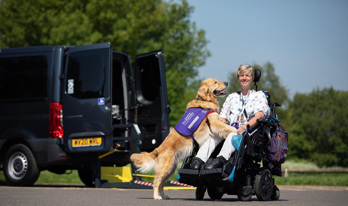 A smiling women in a wheelchair is next to a car with a dog.