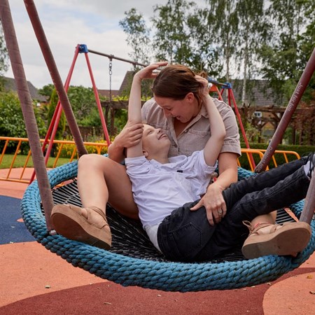 Becci and Lucas are sitting together in a swing, laughing and smiling at one another. 